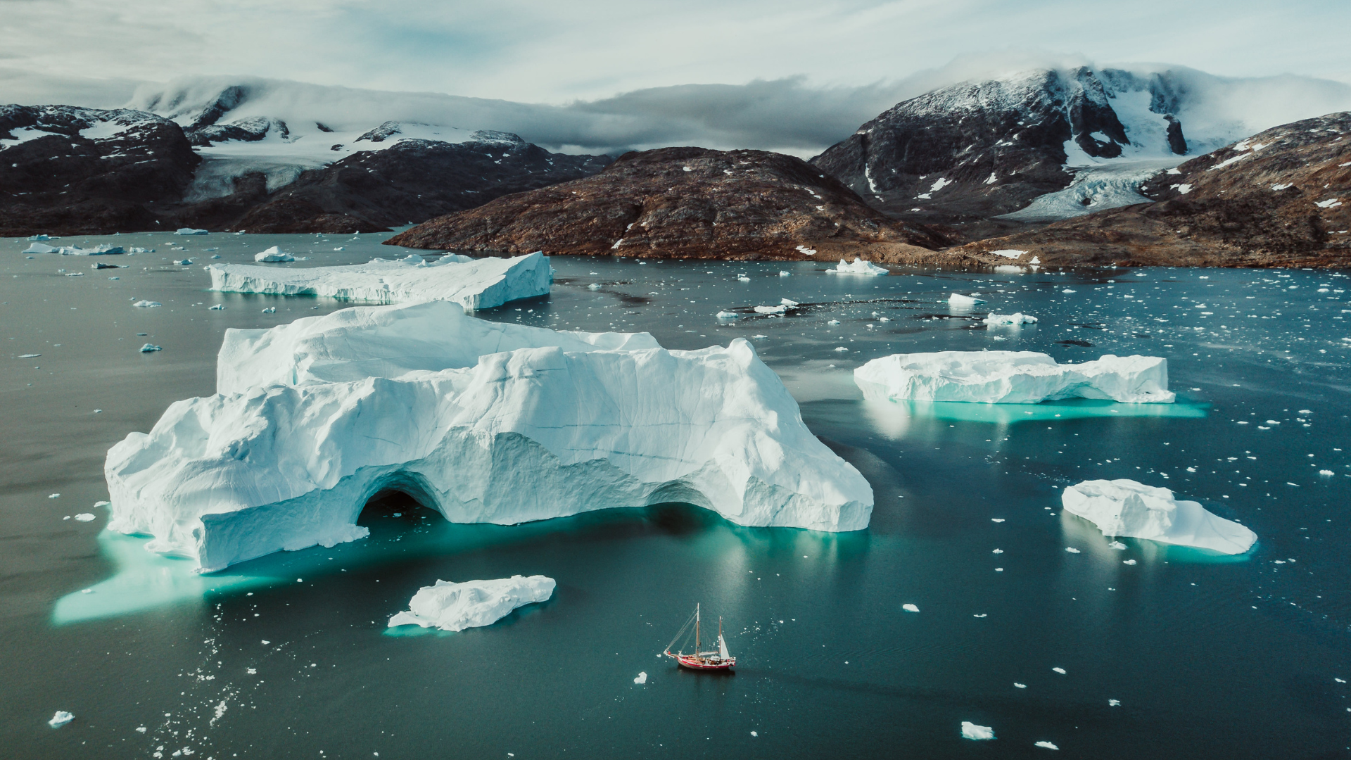 Icebergs in a turquoise Nordic fjord with a small sailboat